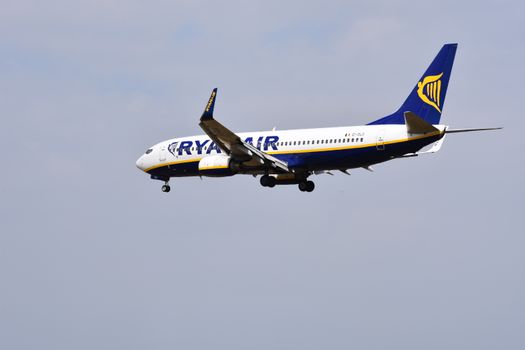 Passagiers bij een Ryanair-vliegtuig op de luchthaven, met handbagage en vertrekschermen op de achtergrond